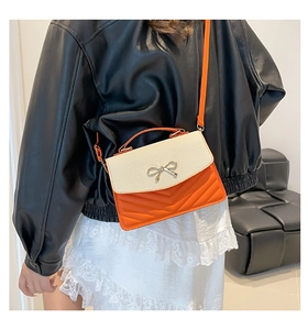 Detail of a chic orange and beige crossbody bag with a metal bow and V-shaped stitching