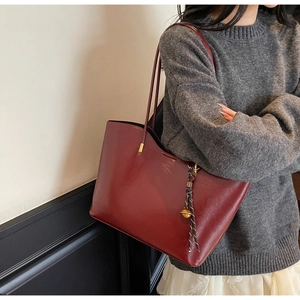 Detail of burgundy leather tote bag with slim straps and golden sphere pendant detail