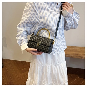 Detail of black quilted leather handbag featuring a golden bamboo handle and turn-lock