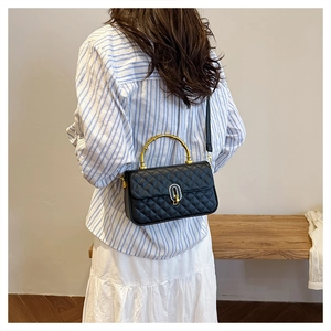 Detail view of black quilted box bag with a golden bamboo handle and turn-lock closure