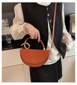 Detail of a brown leather saddle bag with woven texture lid and golden ring handle