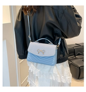 Detail of light blue crossbody bag with gold bow clasp and V-quilted texture on model