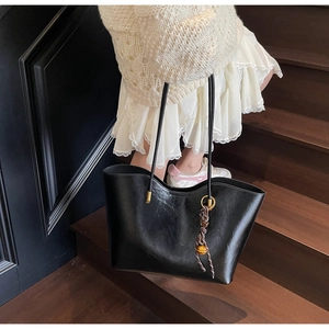 Detail of a large black leather tote bag with elegant gold spherical pendant decoration