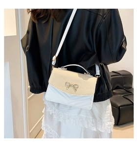 Detail of crossbody bag featuring straw flap, golden bow clasp, and V-quilted leather