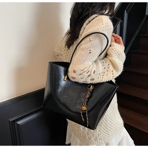 Detail of a large black glossy tote bag featuring a decorative metal charm and slim straps