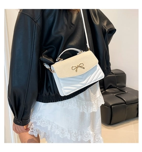 Detail of white quilted crossbody bag with straw flap and golden bow clasp decoration