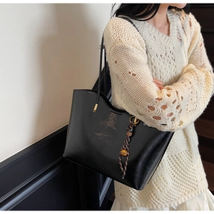 Detail of black glossy leather tote bag with braided pendant and slim shoulder straps