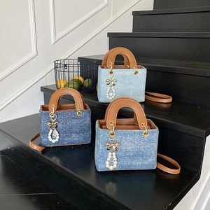 Mini denim lady bag with brown leather trim and pearl bow pendant on black steps