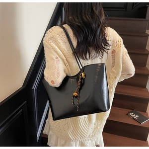 Detail of black glossy patent leather tote bag with gold rings and woven charm on the strap