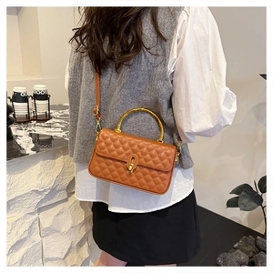 Brown quilted crossbody box bag with gold bamboo handle shown on a model in a modern interior