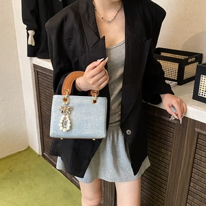 Blue denim crossbody bag with brown leather handles and pearl bow charm accessory