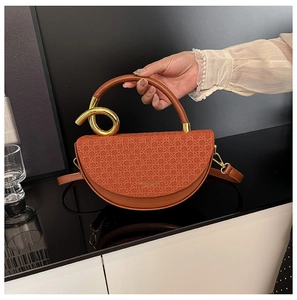 Detail of caramel brown saddle bag featuring woven flap and gold twisted metal handle