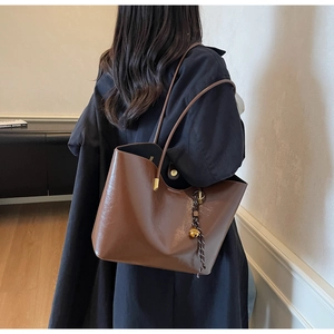 Detail of a brown vintage tote bag showing glossy leather texture and bell charm pendant