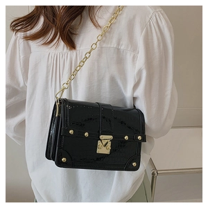 Detail of black crocodile-embossed patent leather bag with gold lock and chain strap