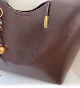 Detail of dark brown tote bag showing smooth oil wax leather texture and gold bell charm