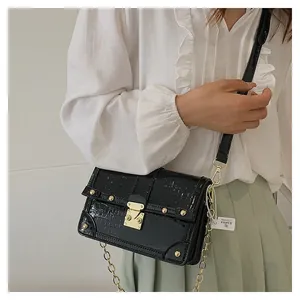 Detail of black crocodile texture bag with gold metal clasp and chain on model