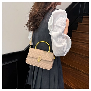 Detail of beige quilted handbag with gold bamboo-shaped handle and oval metal lock closure
