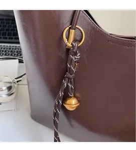 Detailed close-up of dark brown vintage tote bag with decorative gold bell and woven charm
