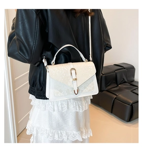 Detail of white crossbody bag featuring snake texture flap and golden buckle on leather jacket