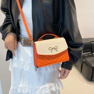 Sac bandoulière orange et beige avec papillon en métal et motif matelassé sur mannequin