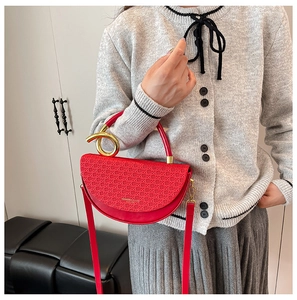 Detail of red semicircular handbag featuring a woven texture flap and golden metal handle