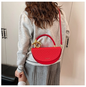 Detail of red textured crossbody bag with golden twisted handle on grey knitwear