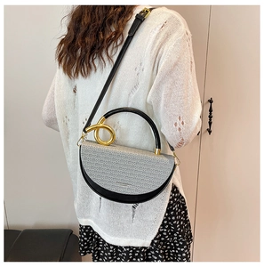 Detail of half-moon crossbody bag with grey woven texture and gold ring handle worn by model
