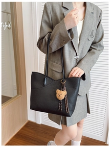 Detail of black lychee grain leather tote bag with brown plush bear charm and long strap