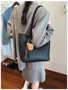 Detail of black lychee grain tote bag with plush bear charm on a female model
