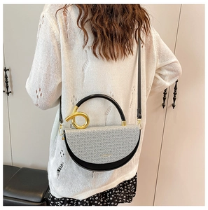 Detail of grey woven texture and black leather saddle bag with golden knot handle