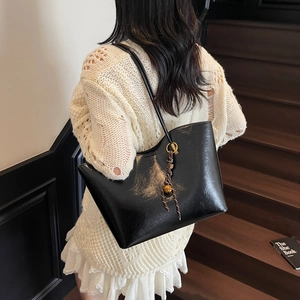 Large black glossy tote bag with decorative tassel shown from a side-view on a model
