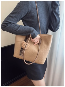 Close-up of khaki pebbled leather tote with brown strap and plush bear charm detail
