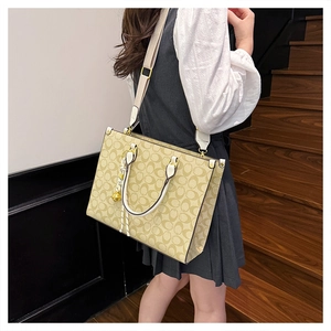 Detail of printed tote bag with broad strap and gold charm shown on wooden stairs