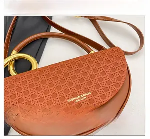 Detail of caramel brown saddle bag featuring a woven leather flap and golden ring handle