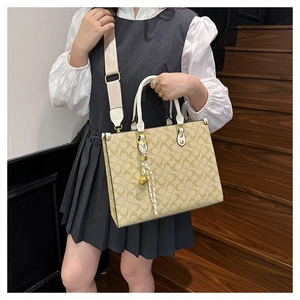 Detail of vintage beige tote bag with monogram print, wide strap, and silk scarf charm