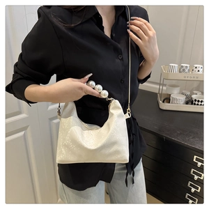 Close-up of white crossbody bag with large pearl handle and gold chain strap detail