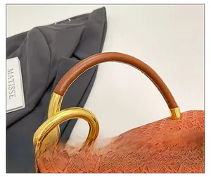 Close-up of woven handbag with twisted gold hardware and leather handle detail
