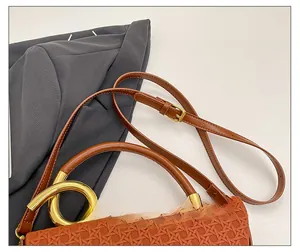 Detail of brown woven texture bag with golden circular handle and adjustable shoulder strap