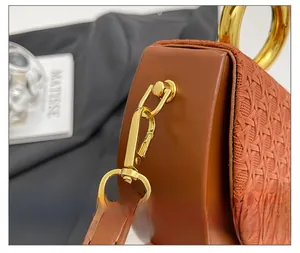 Close-up of golden metal hooks on brown lychee leather and woven fabric handbag