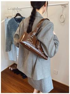 Detail of a brown glossy biker tote bag with silver metal rivets on the side and bottom