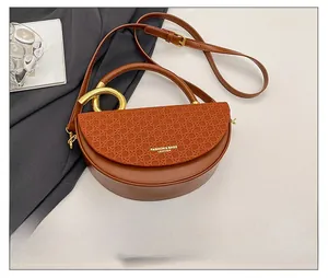 Brown half-moon crossbody bag with leather stitching and gold ring handle detail