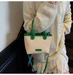 Detail of a beige canvas bucket bag with green leather trim and adjustable strap