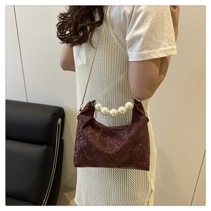 Detail of wine red faux snakeskin handbag featuring a large pearl handle and gold chain strap