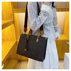 Close-up of printed tote bag with leather handles and gold-tone metal pendant detail