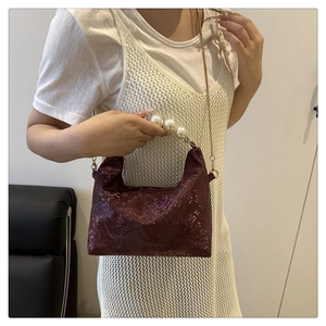 Detail of burgundy snakeskin crossbody bag with large pearl handle and gold chain strap