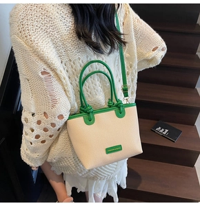 Detail einer beigen geflochtenen Eimertasche mit grünem Lederbesatz und Schultergurt