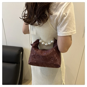 Detail of burgundy snakeskin crossbody bag with pearl handle and golden chain on model