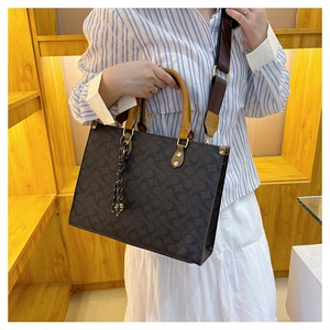 Detail of monogram brown tote bag featuring detachable woven wide shoulder strap and charm