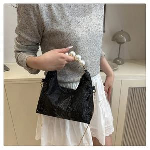Close-up of black faux crocodile texture bag with large pearl handle and gold chain strap