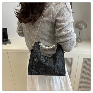 Detail of black python texture handbag with large pearl handle and gold chain strap